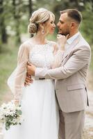 Wedding couple bride and groom walk hand in hand through a pine forest, sunlight filtering through the trees, highlighting their joyful expressions. photo