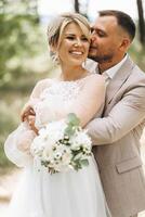 A bride and groom walk hand in hand through a pine forest, sunlight filtering through the trees, highlighting their joyful expressions. photo