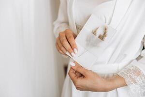 Close-up Bride holds in her hands an envelope with a sheet of paper invitation. Wedding photography, copy space, mock-up. photo