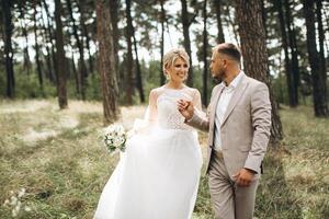 Wedding couple bride and groom walk hand in hand through a pine forest, sunlight filtering through the trees, highlighting their joyful expressions. photo