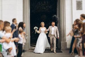 Smiling and happy young married couple leaving church after marriage. Launch of confetti, confetti and flower petals that are good wishes for marriage. photo