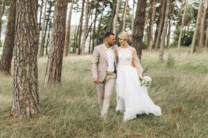 Wedding couple bride and groom walk hand in hand through a pine forest, sunlight filtering through the trees, highlighting their joyful expressions. photo