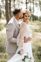 A bride and groom walk hand in hand through a pine forest, sunlight filtering through the trees, highlighting their joyful expressions. photo