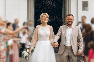 Smiling and happy young married couple leaving church after marriage. Launch of confetti, confetti and flower petals that are good wishes for marriage. photo