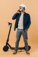 Stylish modern man in a helmet stands by a scooter and talks on the phone photo