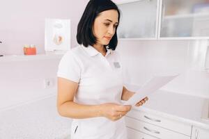 Beautiful female dentist reading work schedule at dental clinic photo