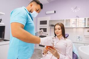 The dentist smiles and shows the girl a model with teeth, talks about implantation and caries. photo