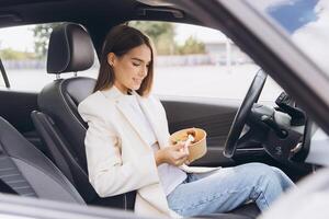 Young Woman Eating Healthy Salad Lunch in Car While Taking a Break From Work, Dressed in Casual Blazer and Jeans on a Relaxing Day photo