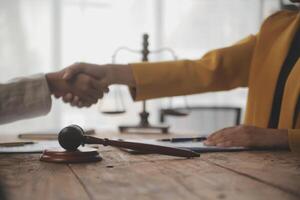 Lawyer shaking hands with a client making about documents, contracts, agreements, cooperation agreements with a female client at the lawyer's desk and a hammer at the table. photo