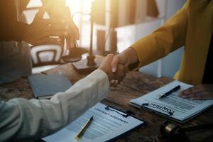 Lawyer shaking hands with a client making about documents, contracts, agreements, cooperation agreements with a female client at the lawyer's desk and a hammer at the table. photo