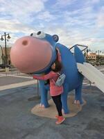 Young woman enjoying a delightful playful moment with a charming blue and pink hippo sculpture found in the playground photo