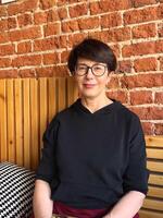 Confident middle-aged woman with glasses sitting against a coffeeshop brick wall. Mature female in casual black hoodie enjoying a relaxing moment Indoors. photo