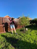 Millennial woman taking photo in a sunny backyard with a small tree and pet dog. Bright and clear blue sky providing a perfect backdrop for outdoor photography. Photographer, connection with nature