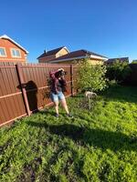 Millennial woman taking photo in a sunny backyard with a small tree and pet dog. Bright and clear blue sky providing a perfect backdrop for outdoor photography. Photographer, connection with nature