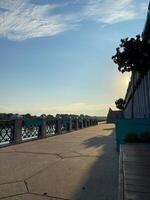 Scenic view of a riverside promenade with blue sky and fluffy clouds. Place leisurely walks and enjoying beautiful weather. Summer time and enjoying nature in urban settings photo