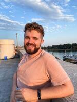 Bearded man gazes thoughtfully at the sunset, leaning against a concrete railing on a scenic promenade. Soft glow of the setting sun creates a serene and reflective atmosphere photo