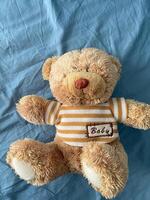 Soft and cuddly teddy bear lies on a light blue fabric surface, exuding warmth and comfort. Timeless design evokes feelings of childhood nostalgia and tranquility innocence photo