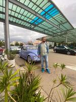 Man standing in front of vintage violet car on the street in summer. Old-fashioned nostalgia and retro style concept photo