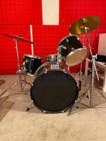 Classic black drum set is positioned in a studio with vibrant red soundproof walls. Shiny black drums and bright red background creates a dynamic and energetic music atmosphere. photo