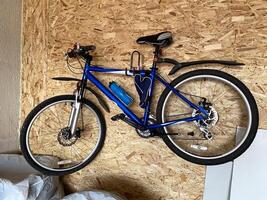 Blue mountain bike is securely mounted on an OSB wooden wall, equipped with a water bottle for the next adventure. Practicality and readiness for outdoor exploration and cycling. photo