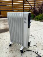White oil-filled radiator stands outside on a concrete surface, prepared to provide warmth on a chilly day. Portable design makes it a practical heating solution for various environments photo