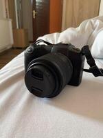 Digital camera rests on a white bed, ready for use, symbolizing creativity and exploration. Relaxed setting suggests a moment of pause before capturing new memories and experiences photo