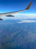 View of airplane wing through window at high altitude, showcasing clear blue sky and clouds far below. Serene beauty of flight and the expansive view of the horizon from above. photo