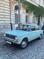 Vintage car is parked on a cobblestone street in front of a historic building adorned with creeping ivy. This classic vehicle evokes nostalgia and charm against the backdrop of timeless architecture photo