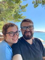 Couple man and woman at the beach under a tree in a sunny day taking selfie for social networks and travel blog. Blogger and journey concept photo