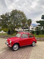 Classic vintage car rests in an urban setting, juxtaposing modern architecture with nostalgic charm. Bright teal vehicle stands out against backdrop of palm trees, photo