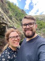 Millennial joyful couple takes a selfie in a lush, mountainous landscape, celebrating their outdoor adventure. Beauty of nature and the happiness of shared experiences photo