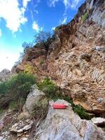 Rugged rock face rises sharply against a backdrop of blue sky dotted with white clouds, showcasing resilience of nature as a lone tree clings to cliffside. Contrast between the harshness of the rocks photo
