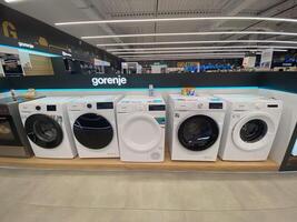 Row of modern washing machines is displayed in an electronics store, showcasing the latest models with sleek designs and advanced features. Under bright lights, photo