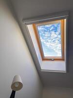 Clear sky view through a skylight reveals a vibrant array of clouds, offering a serene glimpse of outdoors. Wooden frame adds warmth and contrast to the bright blue sky photo