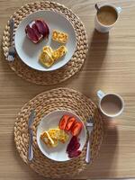 Cozy breakfast setting features plates with cheese, tomatoes, and cured meat, complemented by cups of coffee. Woven placemats and wooden table provide a warm, inviting ambiance photo