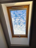Clear sky view through a skylight reveals a vibrant array of clouds, offering a serene glimpse of outdoors. Wooden frame adds warmth and contrast to the bright blue sky photo