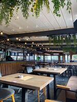 Cozy cafe interior with hanging plants and warm lighting creates a welcoming ambiance. Wooden tables and chairs are arranged neatly, inviting guests to relax and enjoy their time photo