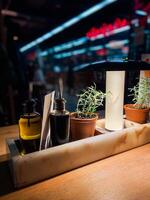 Cozy restaurant table setting with olive oil and balsamic vinegar bottles, flanked by small potted rosemary plants under warm lighting. Blurred background evokes a bustling yet intimate atmosphere photo