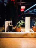 Cozy restaurant table setting with olive oil and balsamic vinegar bottles, flanked by small potted rosemary plants under warm lighting. Blurred background evokes a bustling yet intimate atmosphere photo