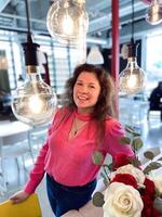 Millennial woman in a vibrant pink sweater sits at table decorated with red and white roses in a modern room. photo
