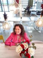 Millennial woman in a vibrant pink sweater sits at table decorated with red and white roses in a modern room. photo