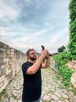 A man takes a photo while standing at a viewpoint in fortress. A tourist with a smartphone camera