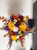 Colorful bouquet of flowers in a lavender box standing on a desk, tied with a vibrant red and purple ribbon. Bright, mixed arrangement adds a touch of nature and warmth to modern workspace photo