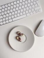Top view white workspace with keyboard and plate of chocolates. The clean, minimal design emphasizes a blend of work photo