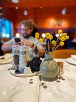 Table with decorative vase and condiment set in cozy restaurant ambiance. Warmth and elegance of a dining table setting, highlighting the intricate details of the decorations photo
