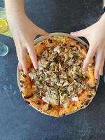 Hands taking slices of freshly baked pizza with chicken and herbs on a dark table. Enjoying a gourmet pizza, emphasizing appetizing toppings and rustic crust photo