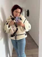 Cozy moment captured as woman holds a Siamese cat and takes a mirror selfie. Dressed in a fluffy jacket and holding smartphone, warm and intimate scene is framed by the hallway background photo