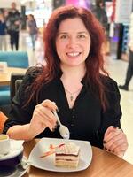 Millennial woman enjoys a sweet dessert in a modern cafe, smiling as she takes a bite. Relaxed atmosphere create a cozy moment for savoring her treat photo
