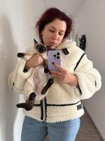 Cozy moment captured as woman holds a Siamese cat and takes a mirror selfie. Dressed in a fluffy jacket and holding smartphone, warm and intimate scene is framed by the hallway background photo