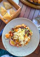 Delicious fresh salad with a variety of vegetables and croutons served on a rustic wooden table. Next to the salad is a wooden box with pieces of bread, creating a perfect meal combination photo